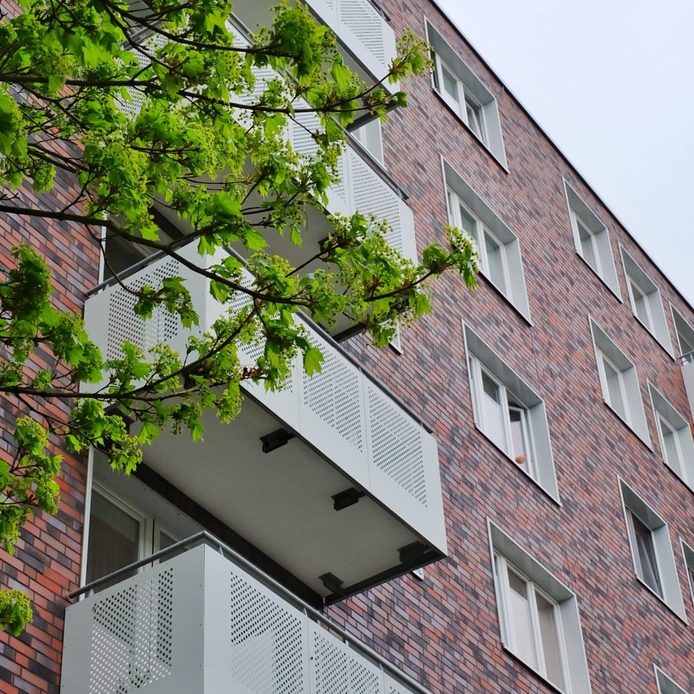 Klinkerfassade mit weißen Lochblech-Balkonen hinter einem Ahornzweig
